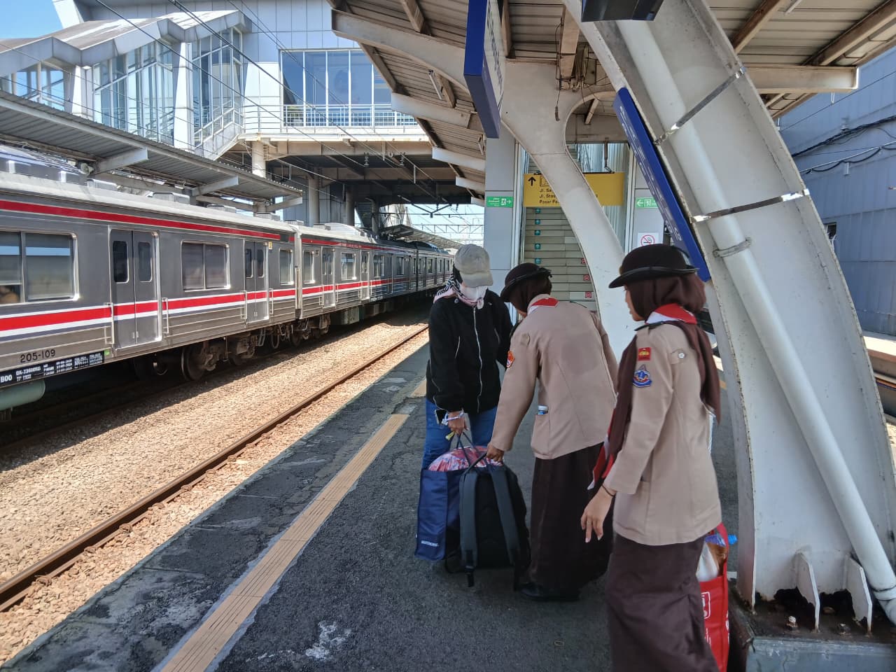 2 anggota pramuka putri membatu penumpang krl yang kesusahan membawa barang